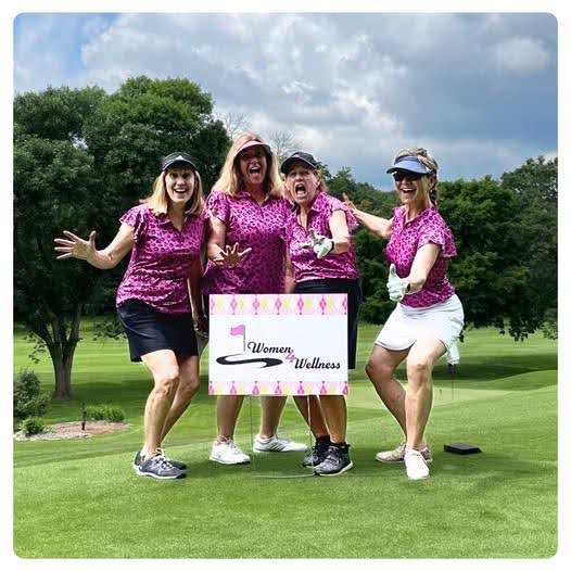 Kayla Hiller with colleagues on the green with event signage from the golf outing